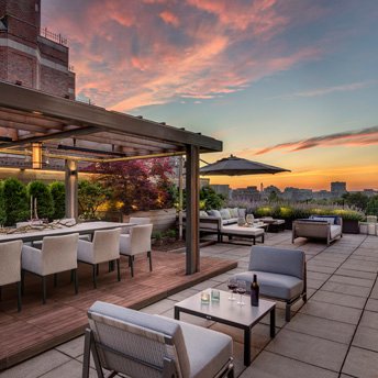 Rooftop terrace with dining pergola, lounge seating, and skyline views at sunset